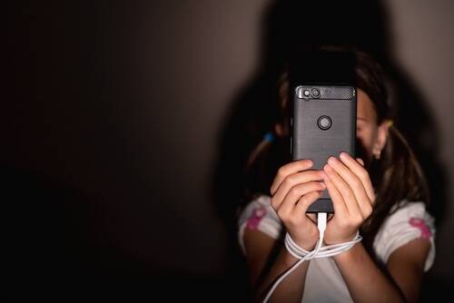 Atlanta Social Media Addiction Lawsuit A young girl holding her phone with her hands wrapped around a cord to signify a social media addiction lawsuit for a child addicted to social media.